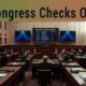 Congressional hearing room with officials and large screens displaying security data.