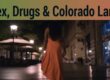 Woman walking alone at night in an urban area, illuminated by streetlights, representing themes of controversy surrounding sex work, drugs, and land disputes in Colorado.